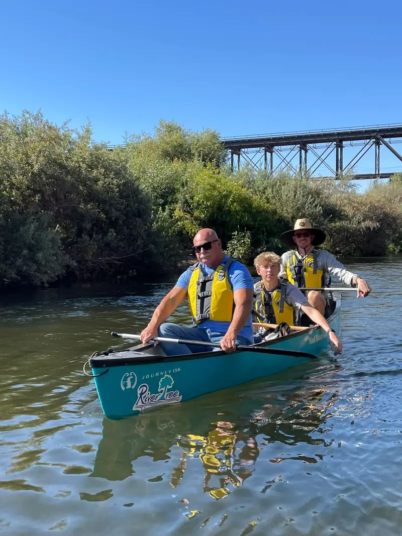Three volunteers paddling a canoe marked with the River Tree logo