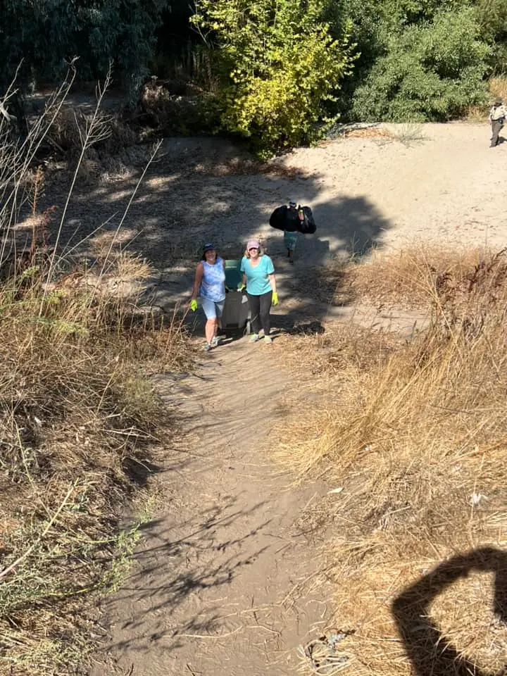 Volunteers hauling a loaded trash bin up the sandy River Bottom Park Trail