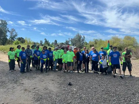 A large crew of volunteers in bright shirts gathered on the riverbank after a cleanup