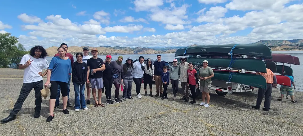A large group of volunteers gathered beside a trailer stacked with canoes before heading out on the water