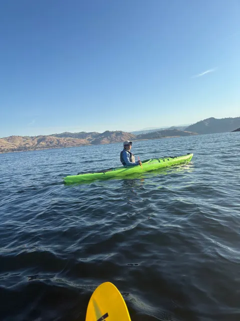 A paddler in a green kayak on open water below the foothills